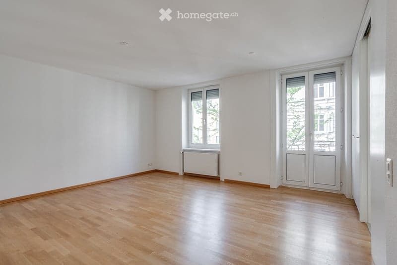 Empty room with wooden flooring, white walls, and large windows. No furniture or equipment present.
