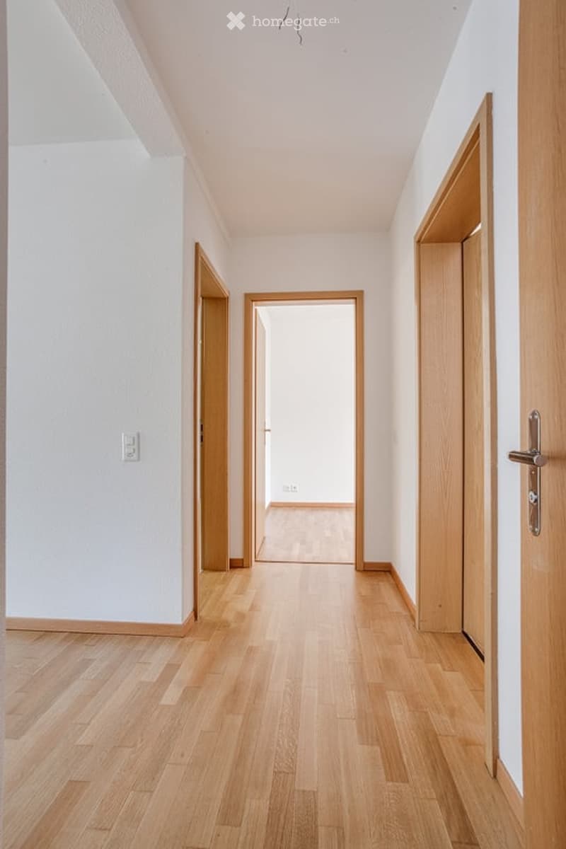 Empty hallway with light wooden flooring, white walls, and open doors leading to other rooms.