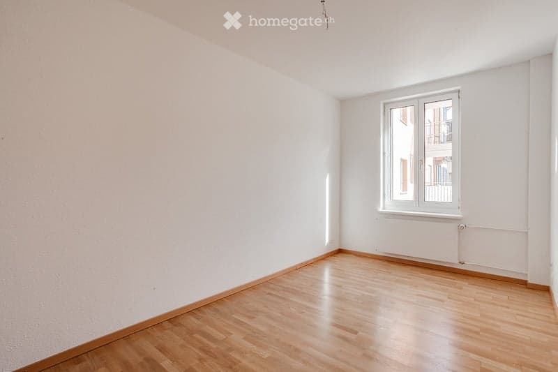 Empty room with light wooden flooring, white walls, and a single window with white frame. No furniture or equipment present.