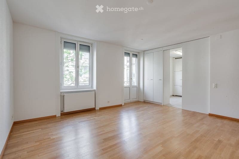 Empty room with wooden flooring, white walls, large windows, and built-in closet. No furniture or equipment present.