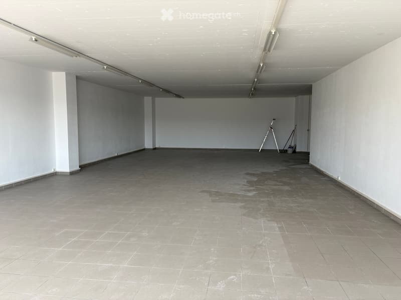 Empty room with white walls, tiled floor, and exposed ceiling with fluorescent lighting. No furniture or equipment present.