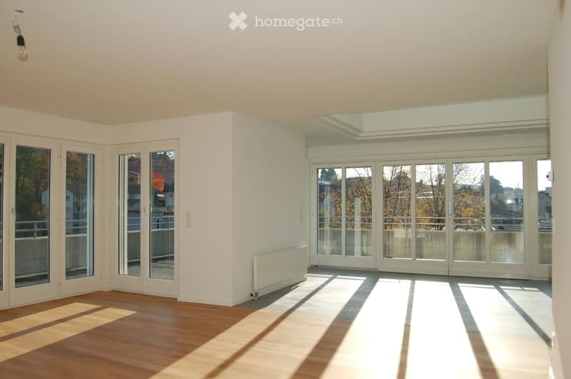 Bright, unfurnished room with wooden flooring, large glass doors leading to a balcony, and a skylight above.
