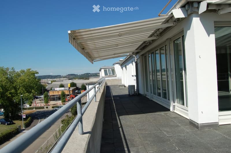 Balcony with a covered awning, metal railing, and a view of the surrounding area including buildings and trees.