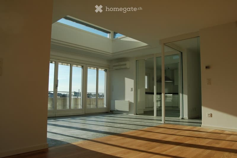Bright, empty room with large glass doors and windows, wooden flooring, and a view of the outside area.