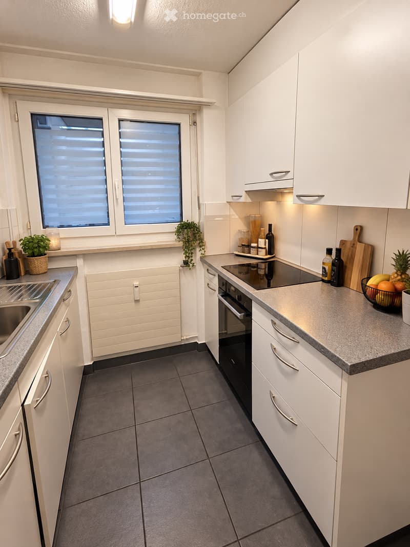 Modern kitchen with white cabinets, stainless steel appliances, and granite countertops. Features include a sink, oven, and various kitchen items on the counter.