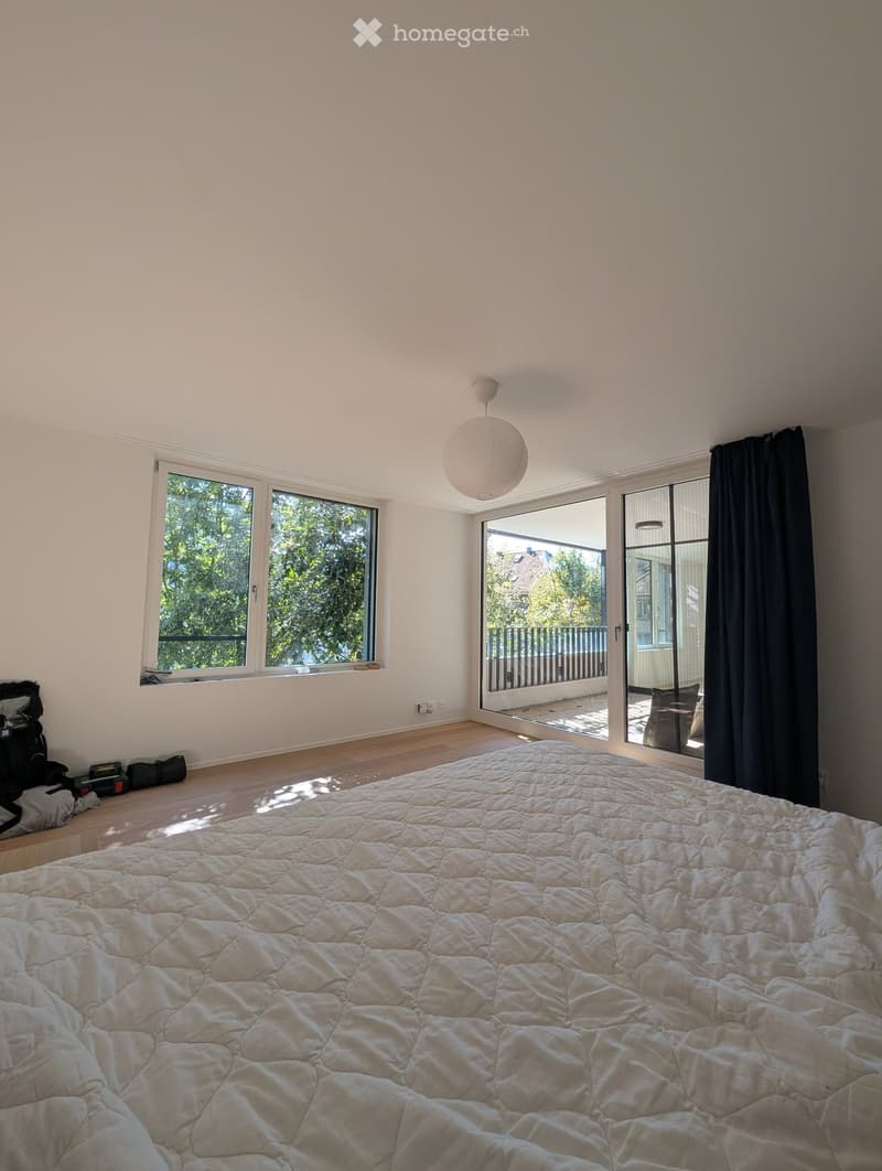 Bright bedroom with large windows, a neatly made bed, and a pendant light fixture.