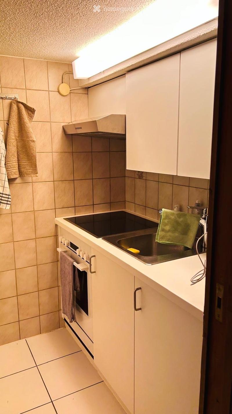 Modern kitchen with white cabinets, stainless steel oven, sink, and range hood. Beige tiled walls and light-colored tiled floor.