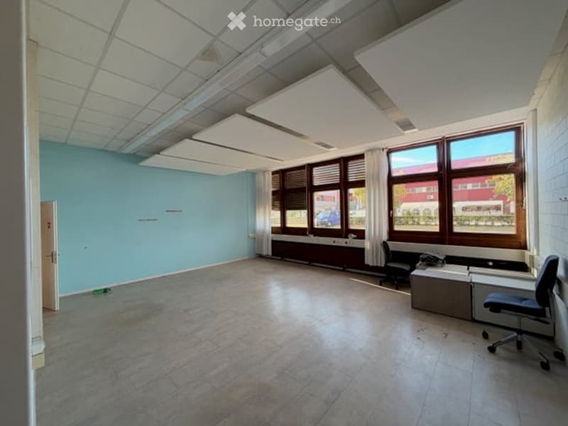 Empty room with light blue walls, large windows with blinds, and a tiled floor. No furniture or equipment present.
