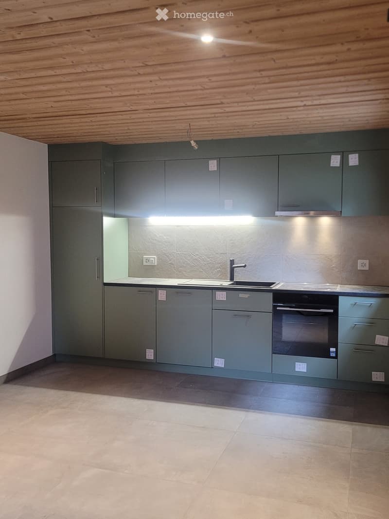 Modern kitchen with grey cabinets, a sink, a faucet, and an oven. The space features a wooden ceiling and tiled flooring.