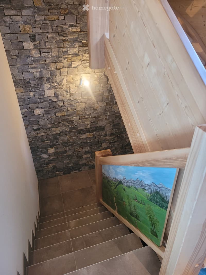 Staircase with wooden handrails and stone walls, featuring a painted mural of a mountain landscape on the landing.