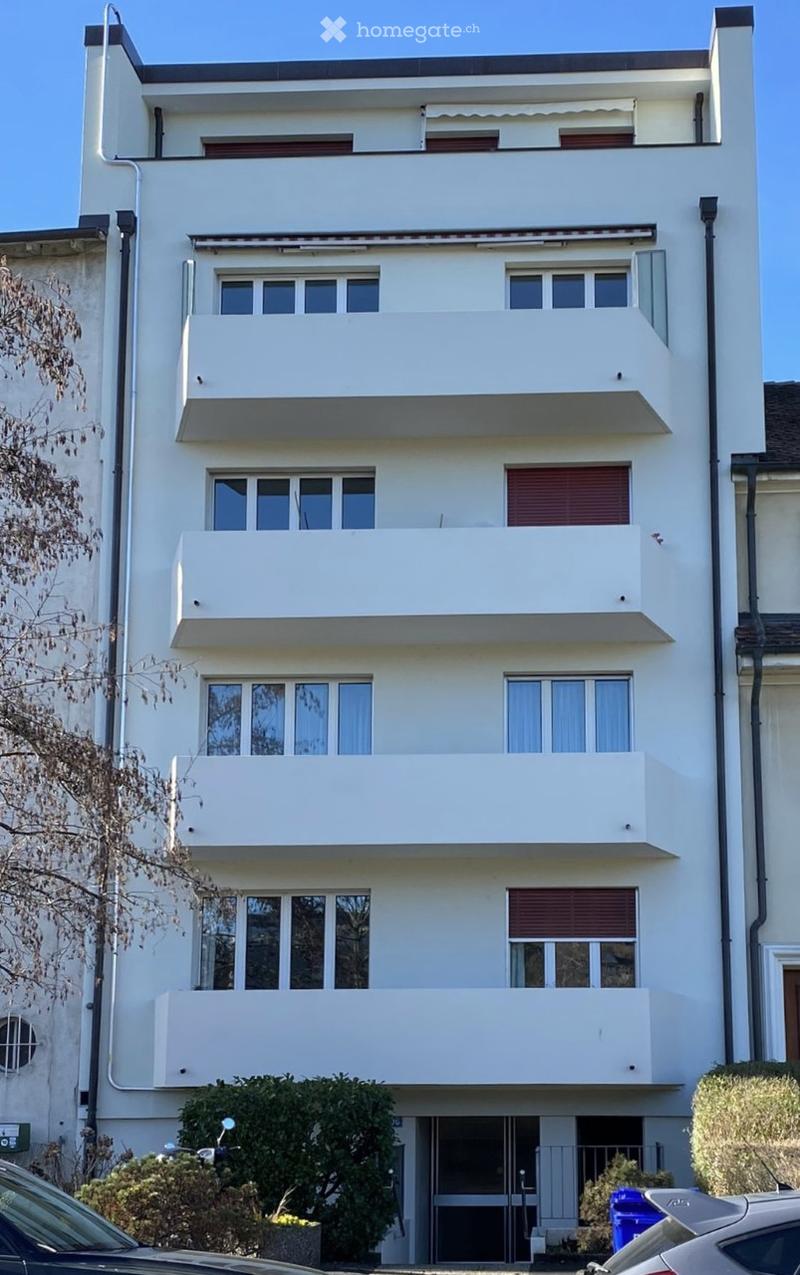 Four-story white building with multiple balconies and large windows, featuring a modern architectural style.