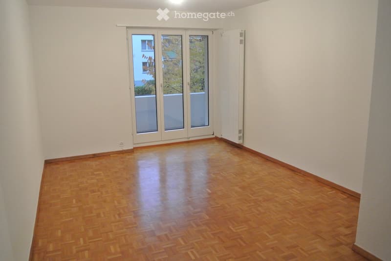 Empty room with wooden flooring, white walls, and large sliding glass doors leading to a balcony.