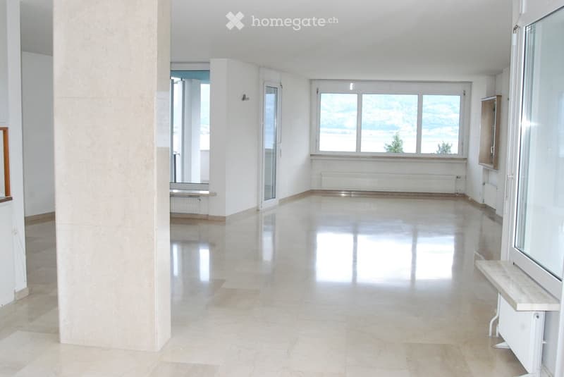 Empty room with white walls, polished tile floor, large windows, and a bench near the window.