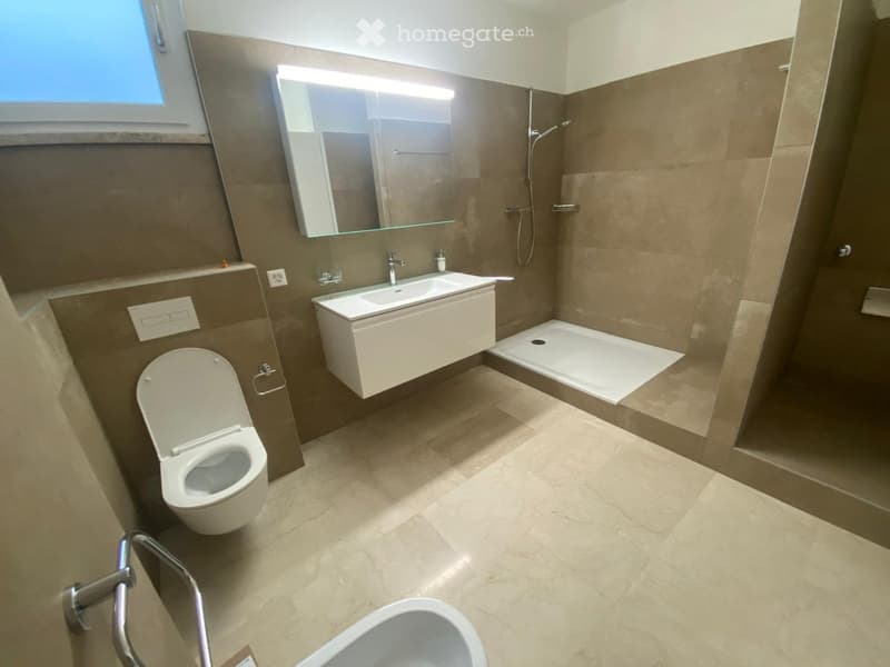 Modern bathroom with beige tiles, a toilet, a sink with a mirror, and a shower area.