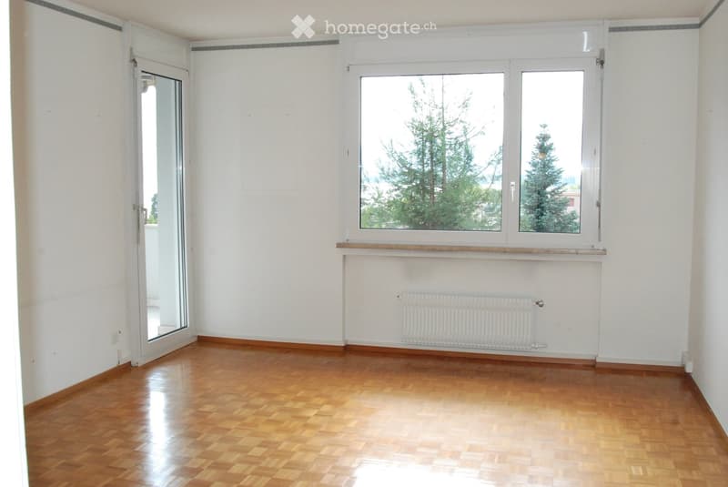 Empty room with wooden flooring, white walls, large windows, and a radiator. No furniture or equipment present.