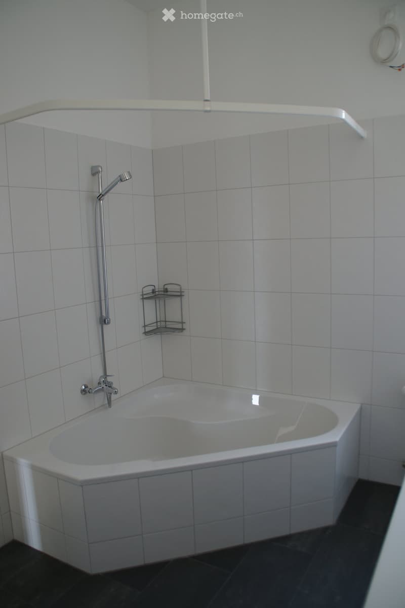 Modern bathroom with a corner bathtub, tiled walls, a showerhead, and a small metal shelf for toiletries.