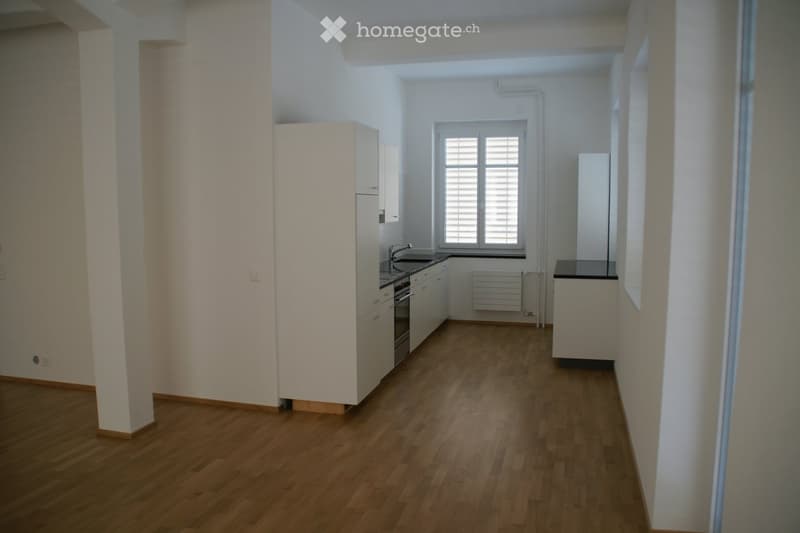 Modern kitchen with light wooden flooring, white cabinets, stainless steel appliances, and a window with blinds.