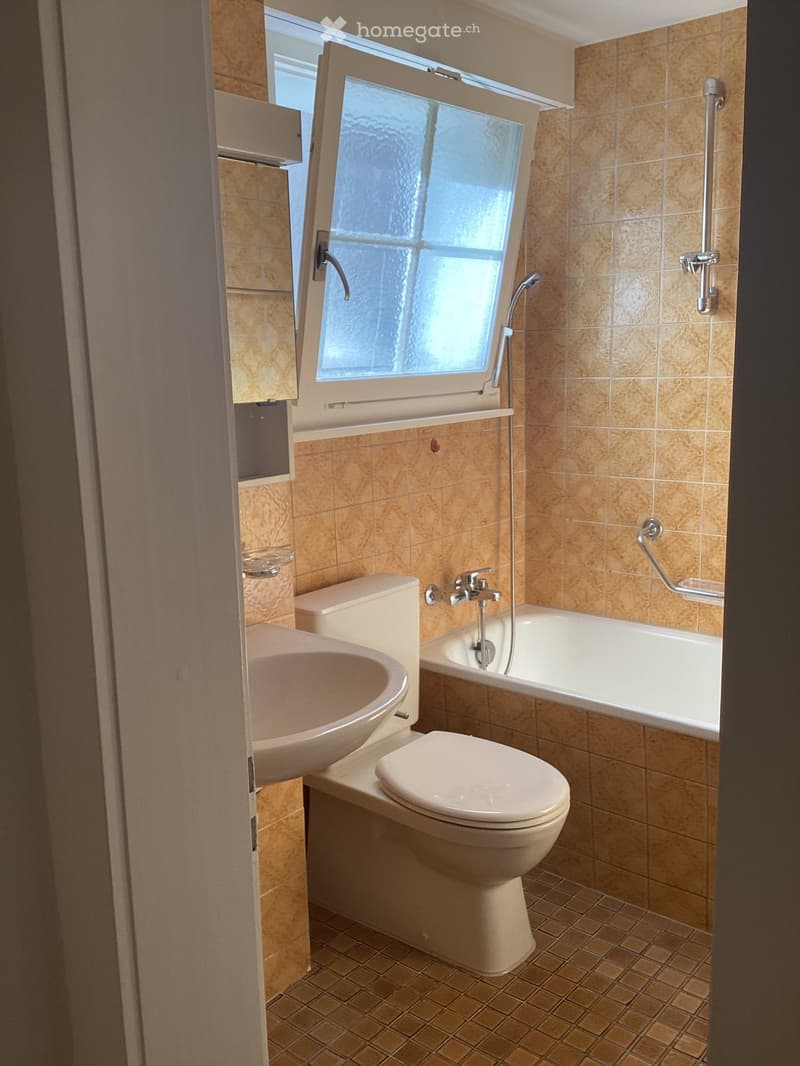 Bathroom with beige tiles, toilet, sink, bathtub, and a window above the bathtub.