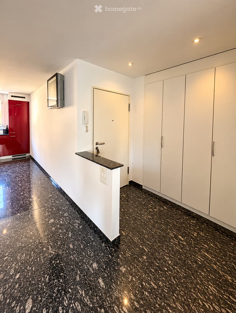 Modern hallway with white walls, black marble flooring, built-in white cabinets, a small black countertop, and a white door leading to another room.