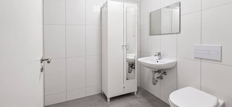 Modern white bathroom with a sink, mirror, cabinet, and toilet. The walls and floor are tiled in white and grey.
