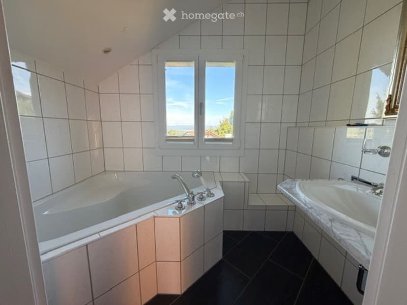 Bathroom with white tiled walls, a bathtub, a sink, and a window offering a view of the sky and trees.