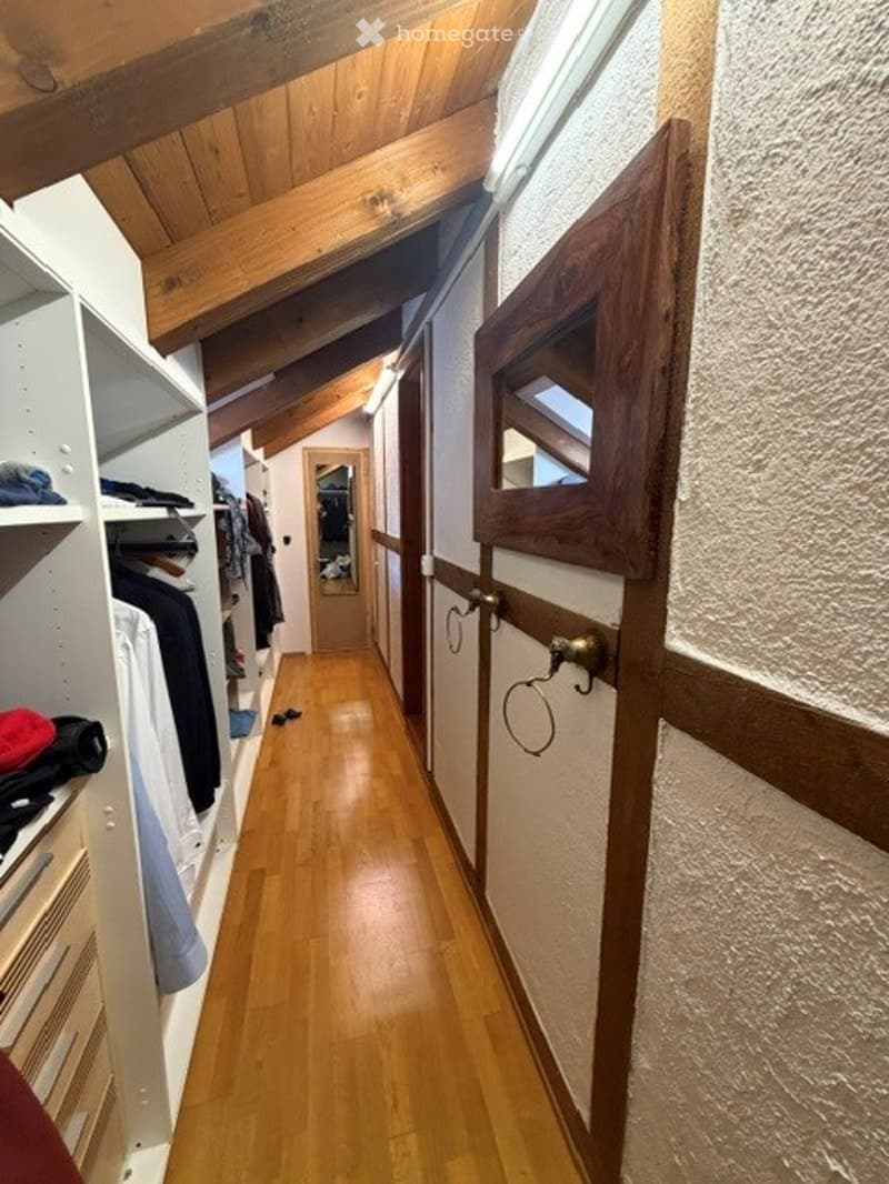 A narrow wooden hallway with slanted wooden ceiling beams, built-in closet on one side, and a mirrored door at the end.