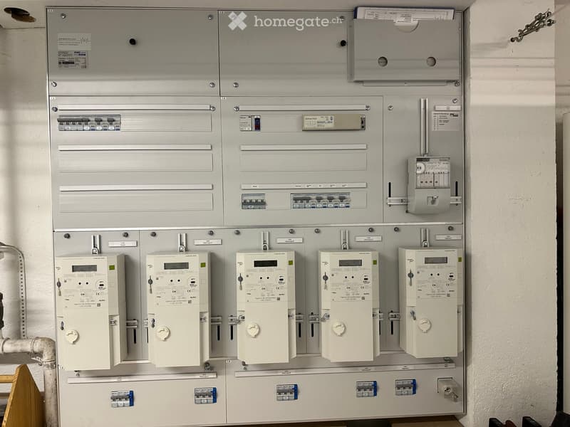 A grey panel with several electrical meters, switches, and circuit breakers installed on a wall.
