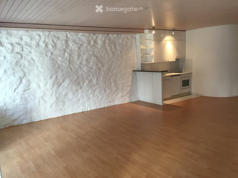 empty room with wooden floor, white wall, kitchen area with oven and countertop