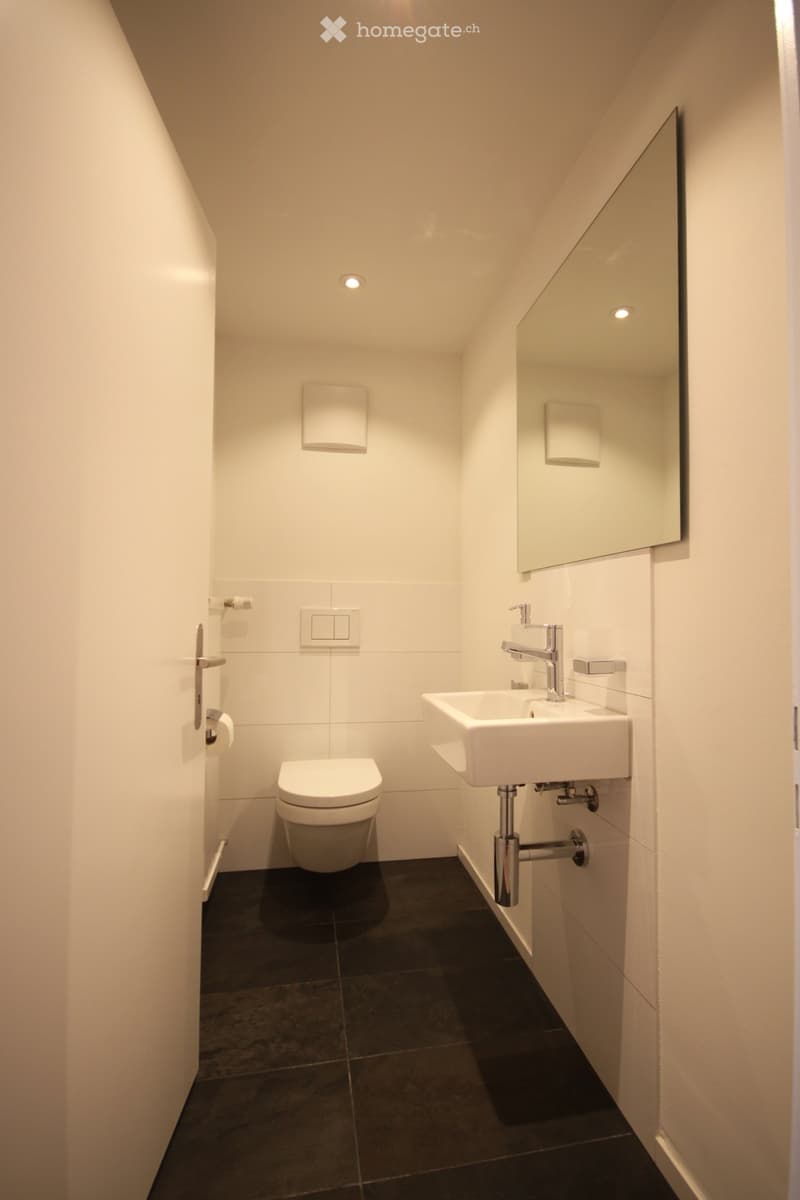 modern, minimalist design with white tiles, a toilet, a sink, a mirror, and a silver faucet