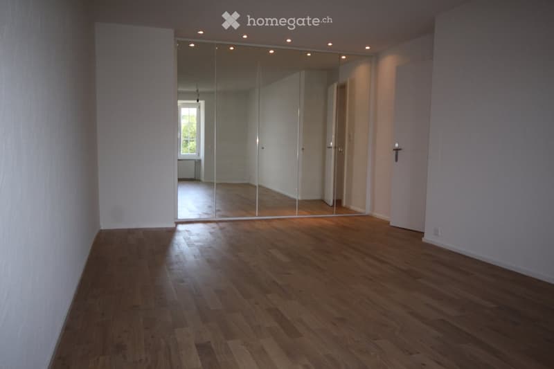 large mirrored wardrobe, hardwood floors, large white walls, a door at the back of the room