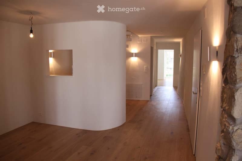 Hallway with wooden floor, white walls, large curved feature wall, recessed lighting, and wall mounted lights