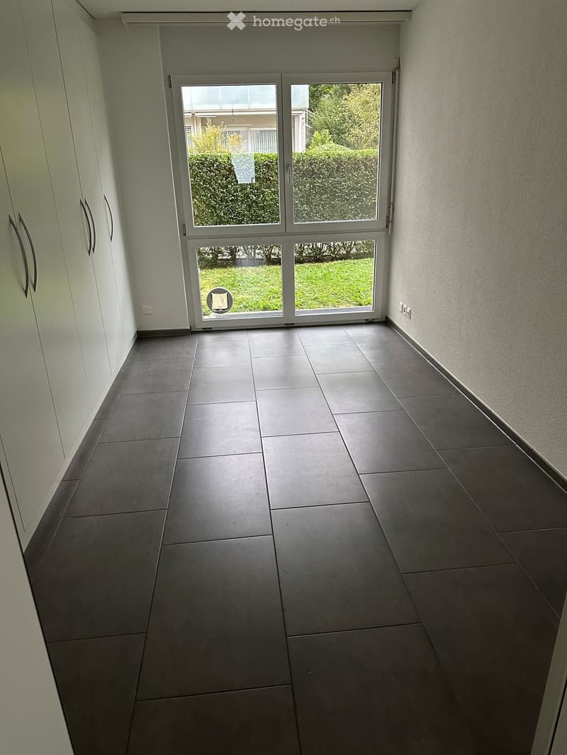Empty hallway with tiled floor, white walls, and a sliding glass door leading to a green outdoor area.