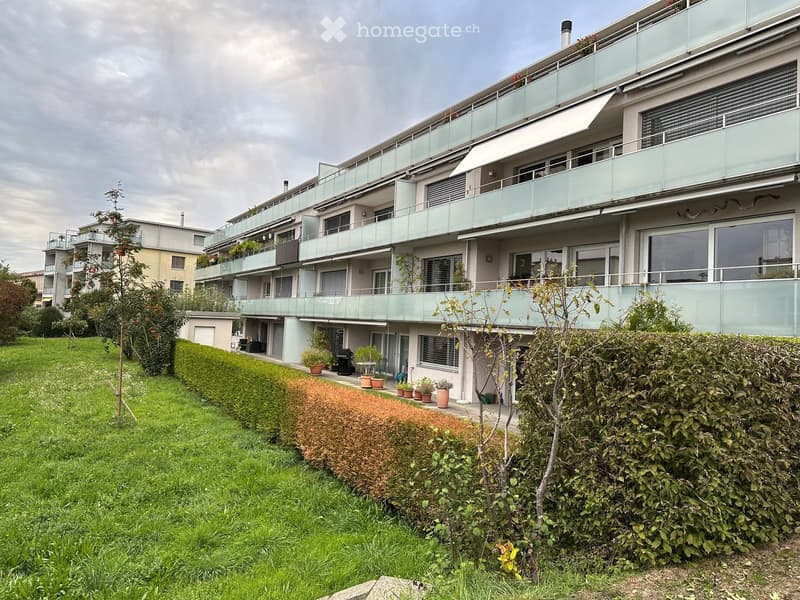 Modern multi-story residential building with balconies, large windows, and surrounding greenery.