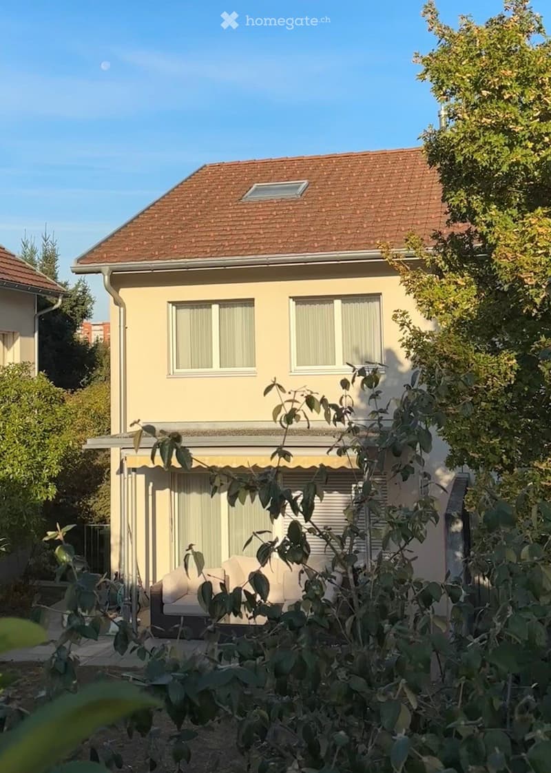 Two-story house with beige exterior, red-tiled roof, and covered patio area with outdoor seating.