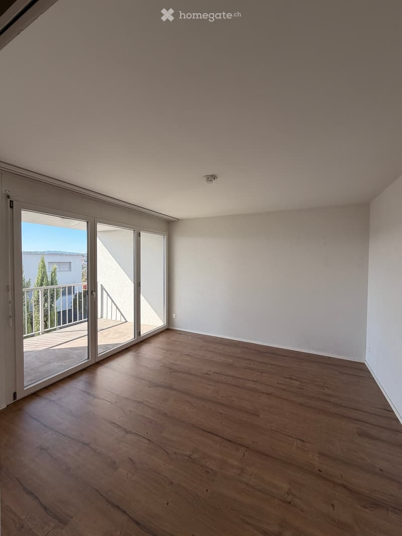 Empty room with wooden flooring, white walls, and large sliding glass doors leading to a balcony.