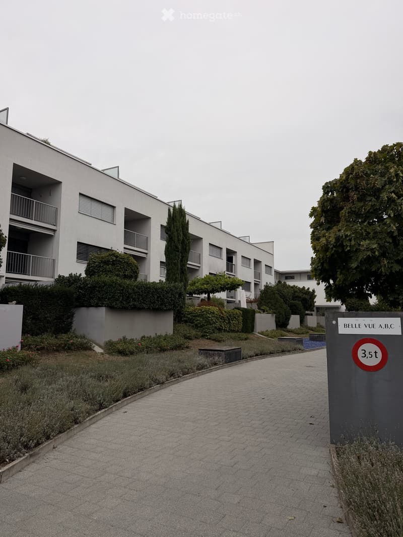 Modern multi-story residential building with balconies, surrounded by landscaped gardens and pathways.