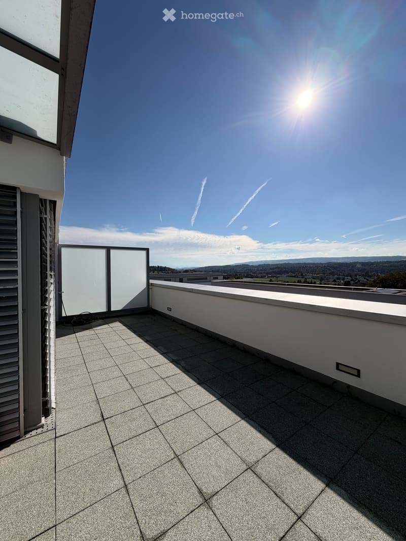 Roof terrace with tiled flooring, white walls, and a clear view of the surrounding landscape under a bright blue sky.
