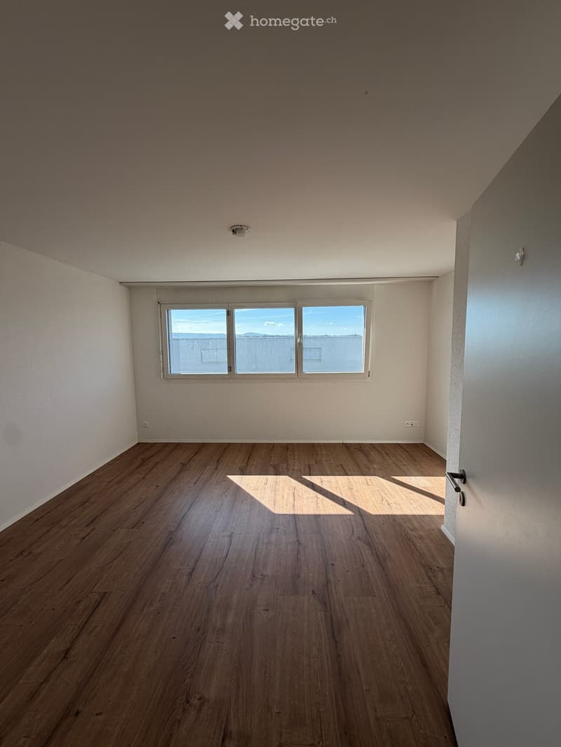 Empty room with wooden flooring, white walls, and large windows offering a view of the outside. No furniture or equipment is present.
