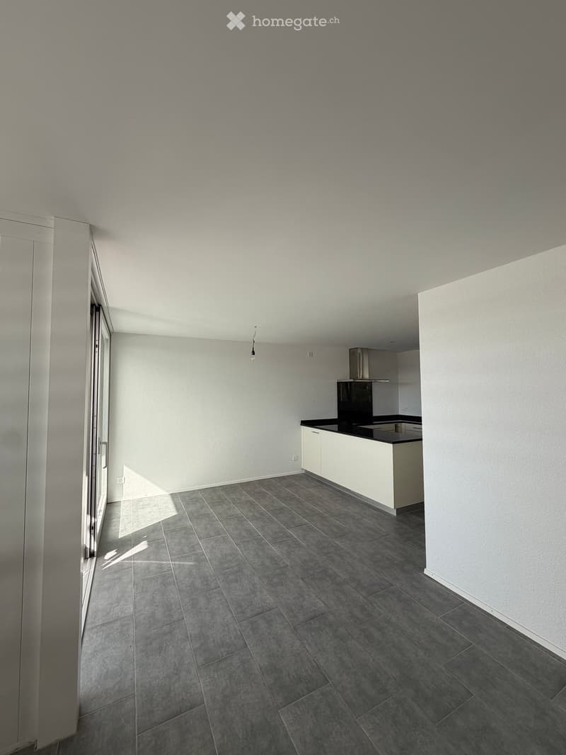Modern kitchen with grey tiled floor, white cabinets, and a black countertop. The space is well-lit with natural light from a large window on the left side.