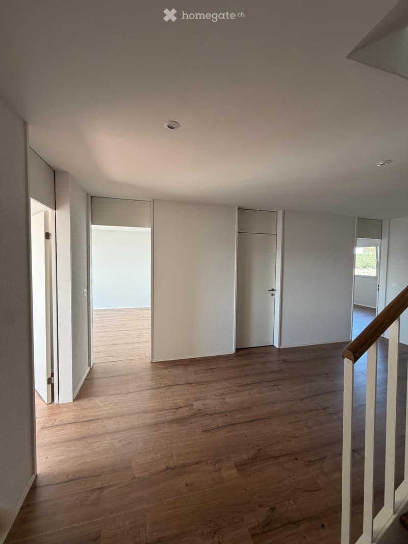 Empty hallway with wooden flooring, white walls, and several closed doors leading to other rooms.
