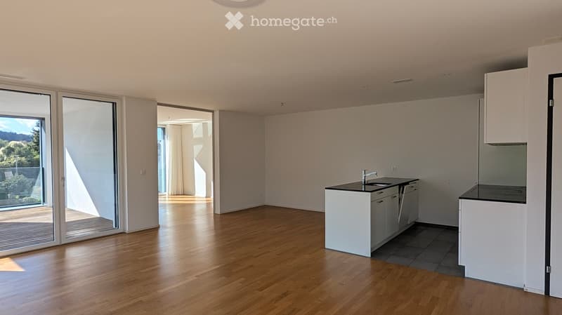 Bright, open kitchen with wooden flooring, white cabinets, and a modern kitchen island. Large sliding glass doors lead to a balcony with a scenic view.