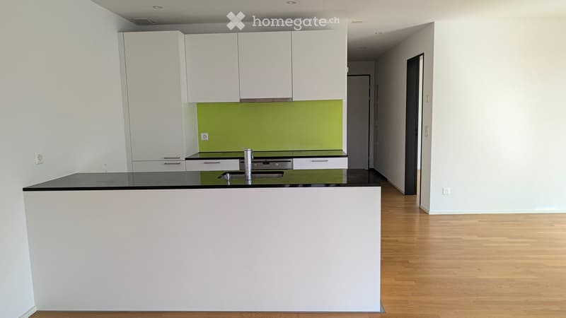Modern kitchen with white cabinets, black countertops, and a green backsplash. Features a central island with a sink and faucet.