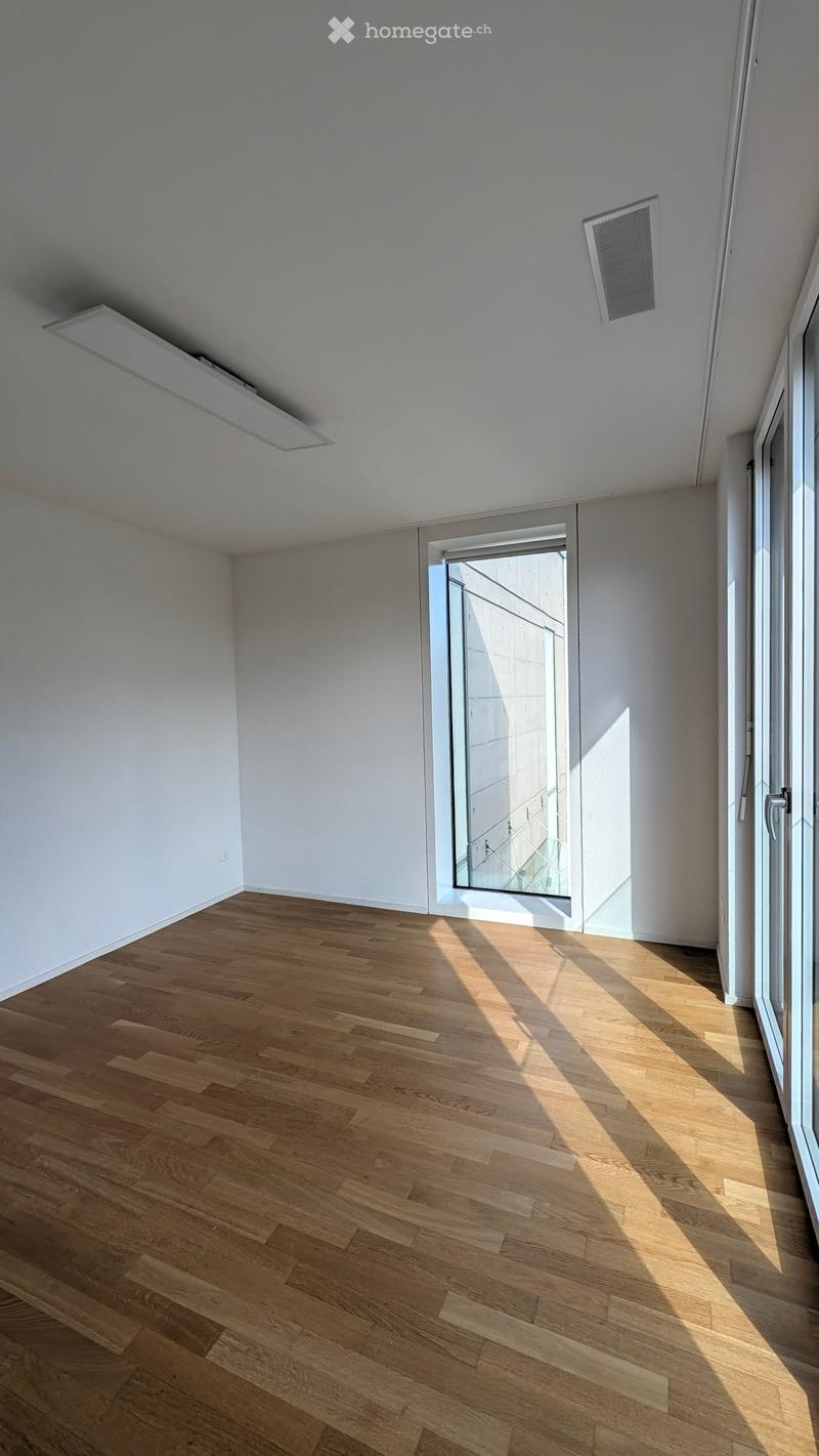 Empty room with light wooden flooring and white walls, featuring a large glass door and window allowing natural light to enter.