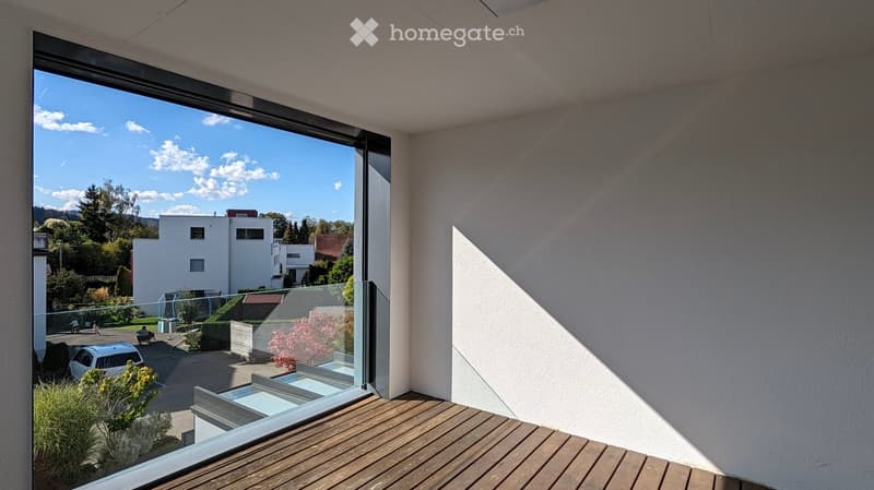 Modern balcony with wooden decking, large glass windows, and a view of a residential area with houses, trees, and a parked car.