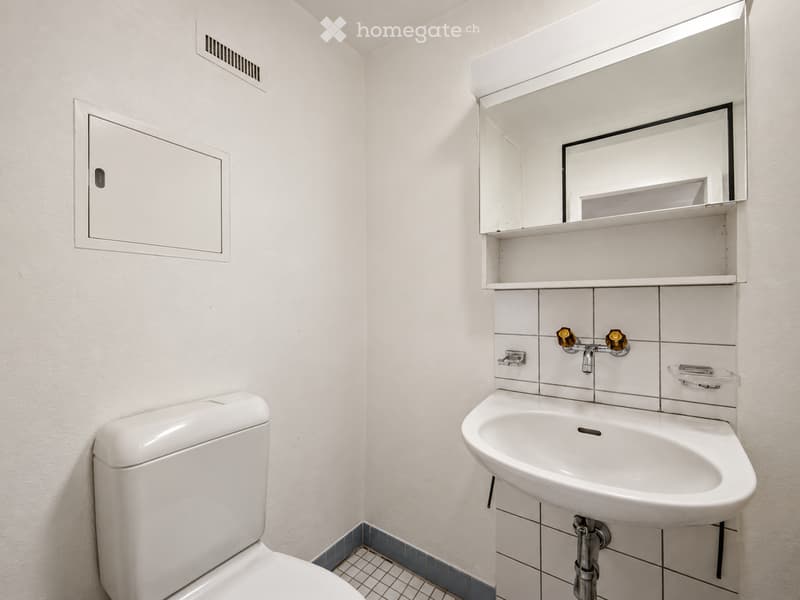 Modern bathroom with white tiled walls, a toilet, a sink with a mirror cabinet, and a small cabinet on the wall.