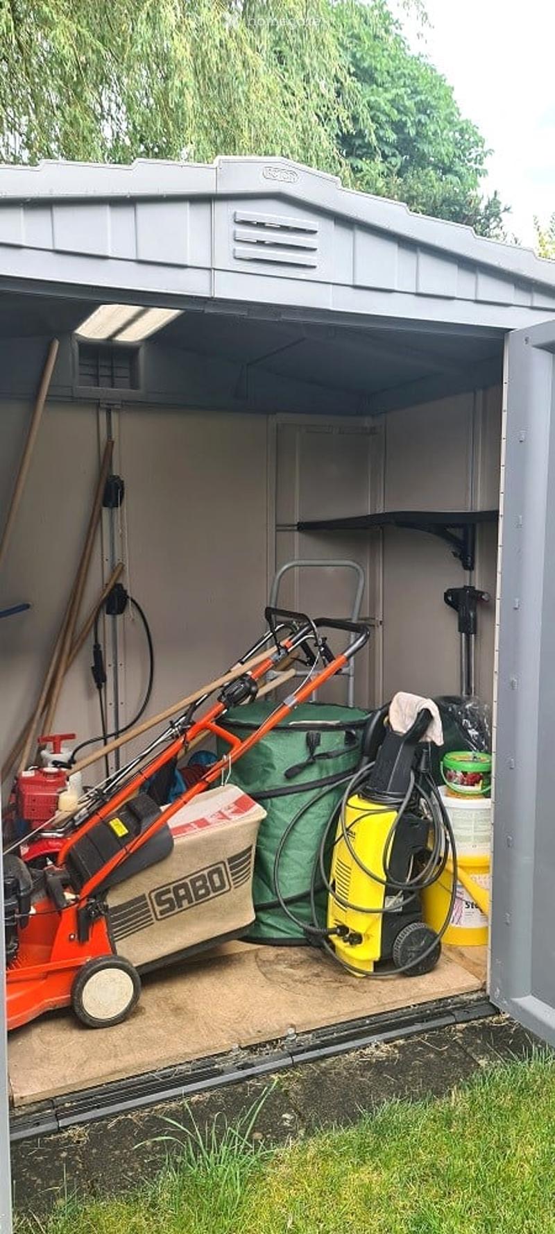 A storage shed with a lawn mower, pressure washer, garden tools, and storage boxes inside.