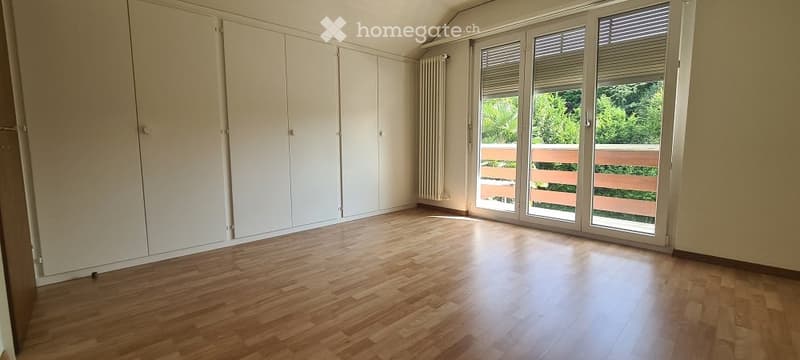 Empty room with wooden flooring, white built-in wardrobes, and large sliding glass doors leading to a balcony.