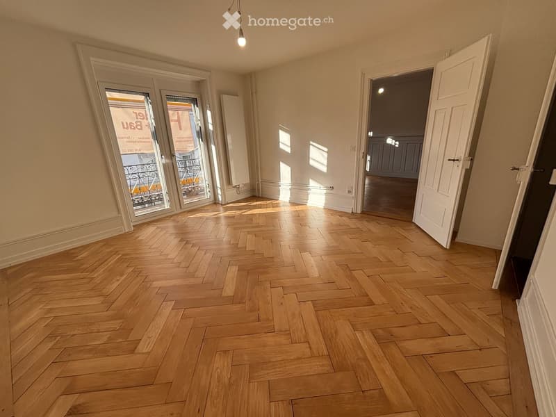 Empty room with wooden herringbone flooring, white walls, and large glass doors leading to a balcony.