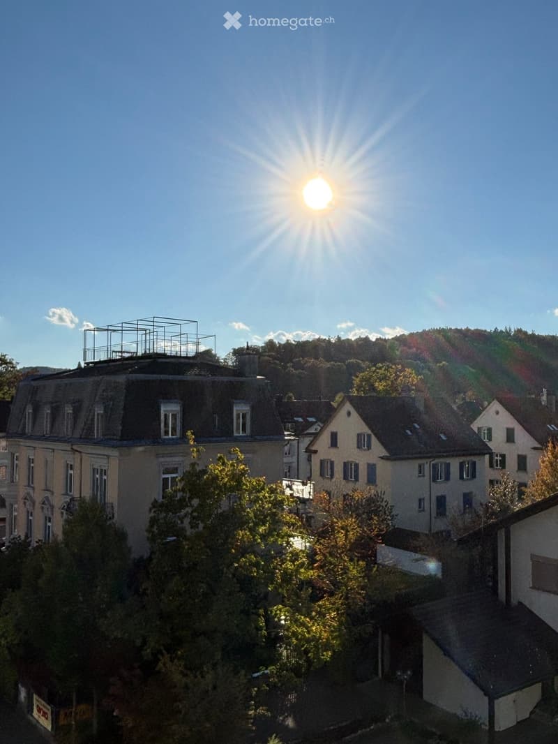 A view of a residential area with multiple buildings, trees, and a clear blue sky with the sun shining brightly.