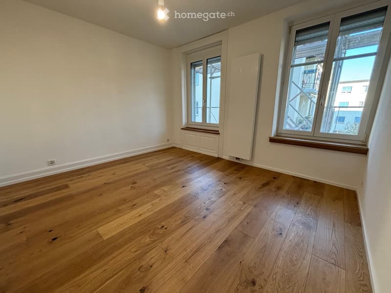 Empty room with wooden flooring, white walls, and large windows with wooden sills. No furniture or equipment present.